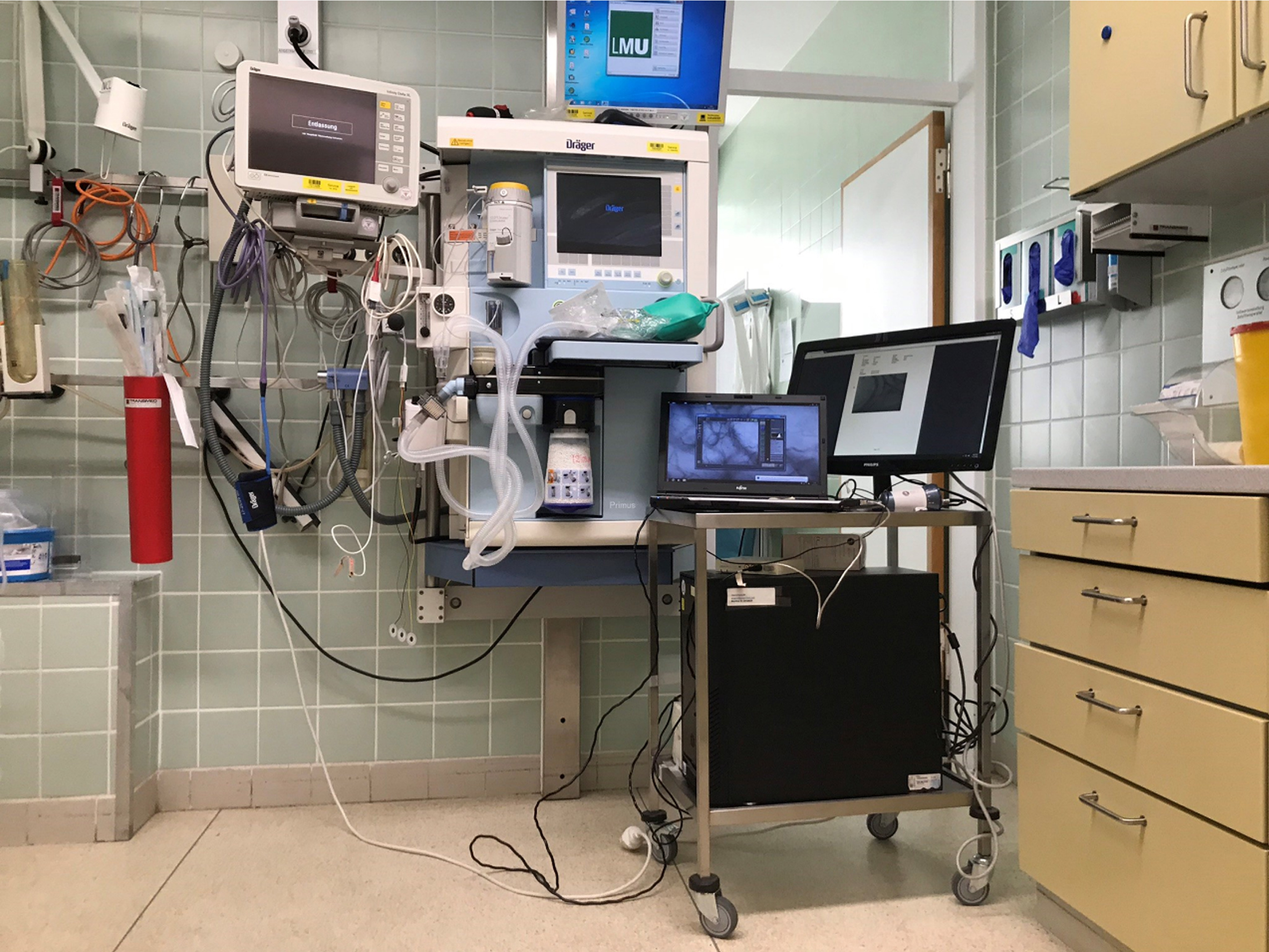 Picture of the anesthesia induction room with the “microcirculation-imaging unit” including SDF-camera, computer, and monitor. To allow flexible recordings and changes between different locations (induction room, operating room, PICU), the equipment was placed on a mobile instrument card and provided with an uninterruptible power supply.